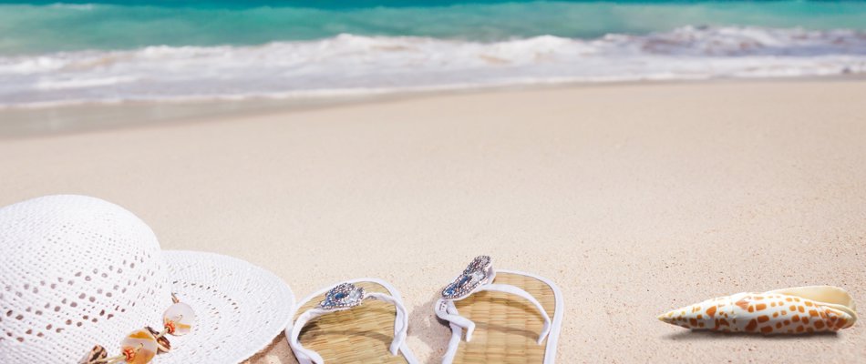 Sandstrand med solhat, sandaler og en konkylie
